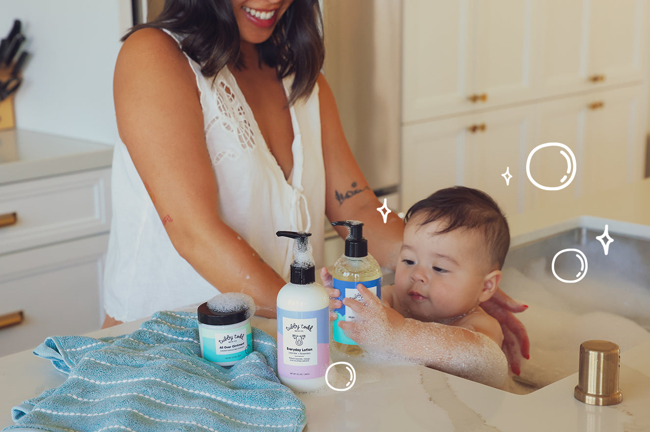 Woman with a baby in a bathtub with various Tubby Todd products on the edge of the tub.